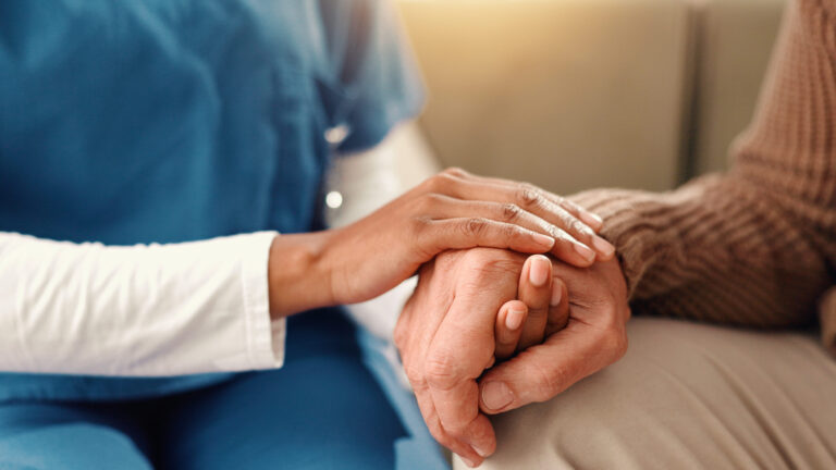 Close-up of a healthcare worker's hand comfortingly holding a patient's hand.