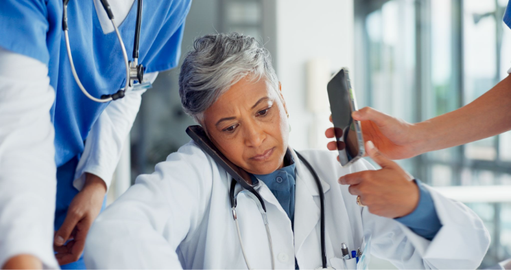 A female doctor on a phone call while another medical professional holds a smartphone nearby.
