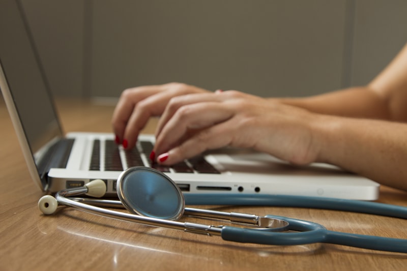 Healthcare professional typing on a laptop with a stethoscope, representing clinical workflow and digital healthcare solutions